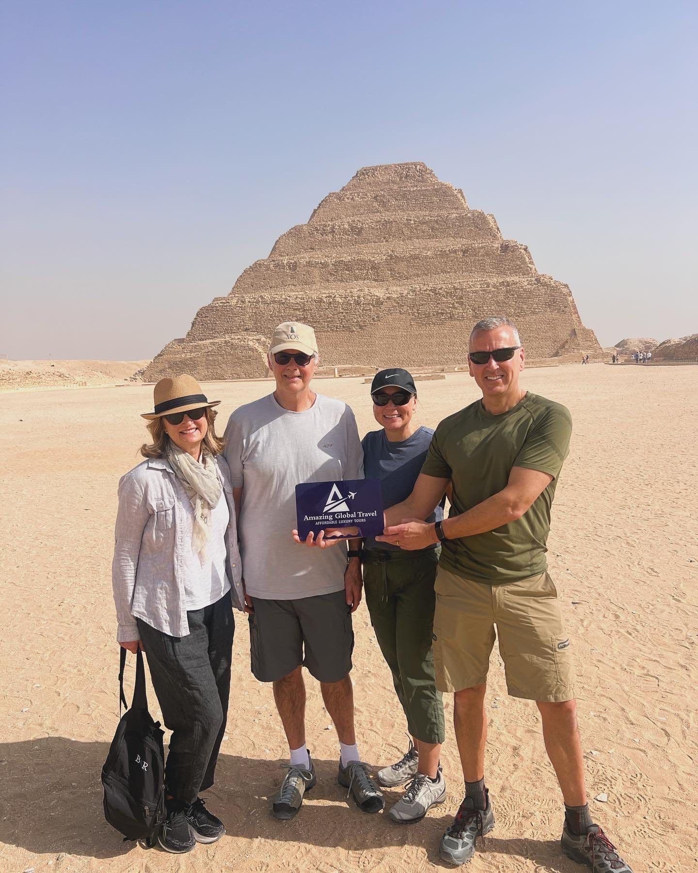 Four travelers holding an Amazing Global Travel sign before the Step Pyramid